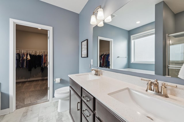 full bathroom featuring double vanity, a stall shower, a sink, and toilet