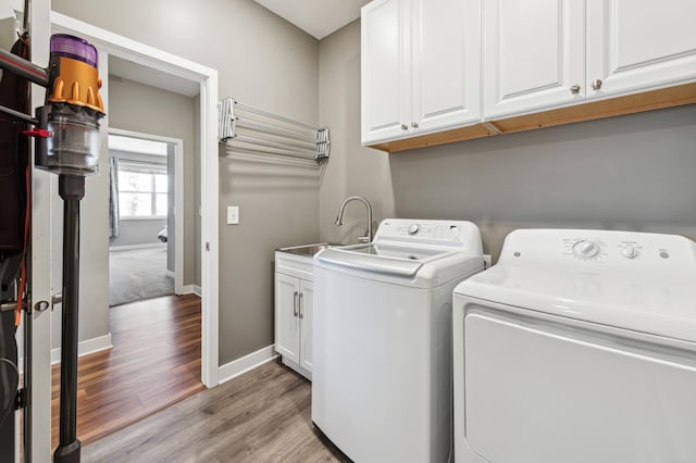 washroom featuring washer and clothes dryer, cabinet space, light wood-style flooring, a sink, and baseboards