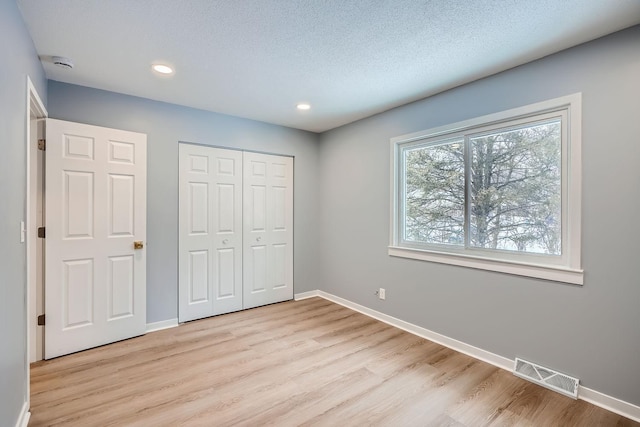 unfurnished bedroom with light wood-type flooring, a textured ceiling, and a closet