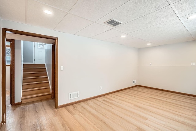 spare room with a drop ceiling and light hardwood / wood-style flooring