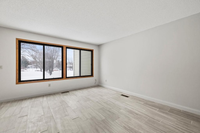 empty room featuring a textured ceiling, light wood-type flooring, visible vents, and baseboards