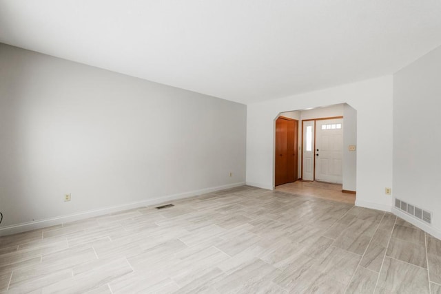 empty room with baseboards, visible vents, and arched walkways