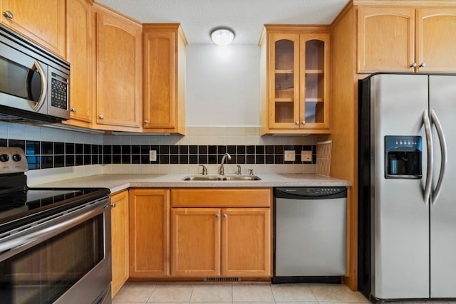 kitchen with a sink, light countertops, appliances with stainless steel finishes, tasteful backsplash, and glass insert cabinets