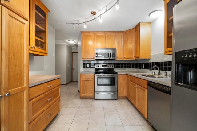 kitchen with decorative backsplash, glass insert cabinets, appliances with stainless steel finishes, light countertops, and a sink