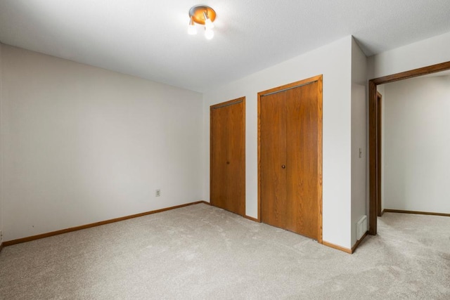 unfurnished bedroom with multiple closets, light carpet, and baseboards