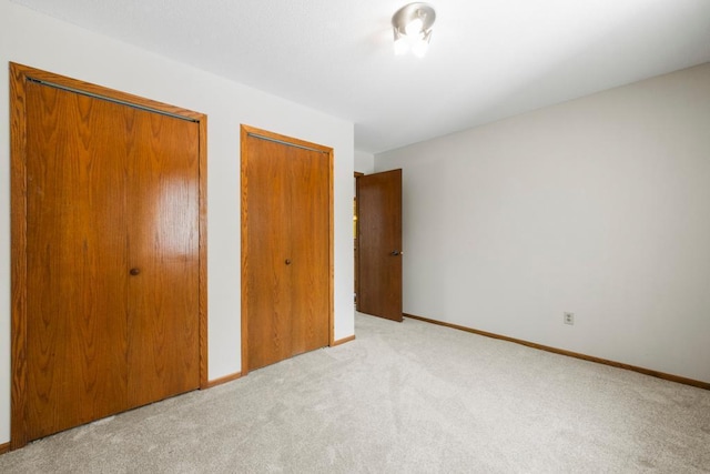 unfurnished bedroom with light carpet, two closets, and baseboards