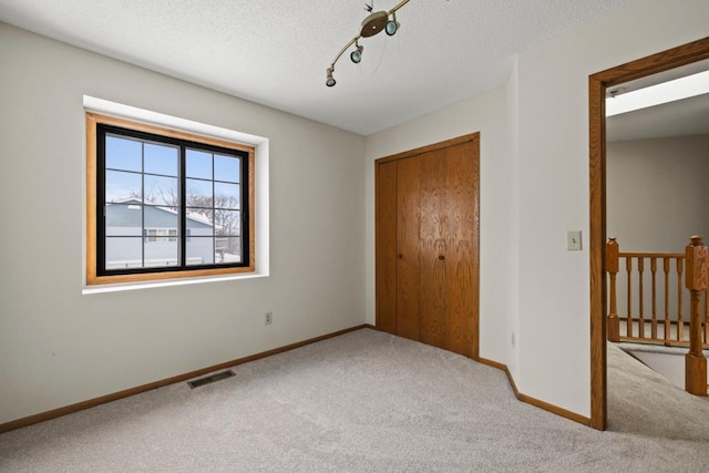 unfurnished bedroom featuring carpet, a textured ceiling, visible vents, and baseboards