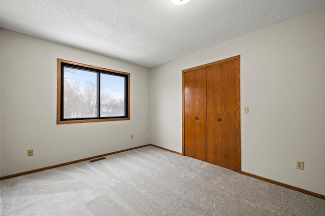 unfurnished bedroom featuring a textured ceiling, a closet, baseboards, and light colored carpet