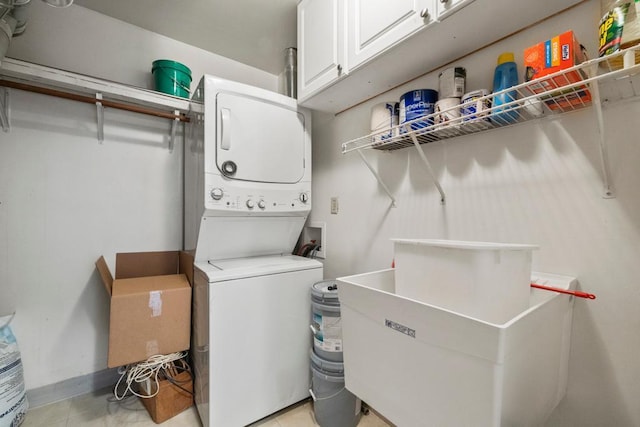 laundry room with a sink, cabinet space, light tile patterned floors, and stacked washer / drying machine