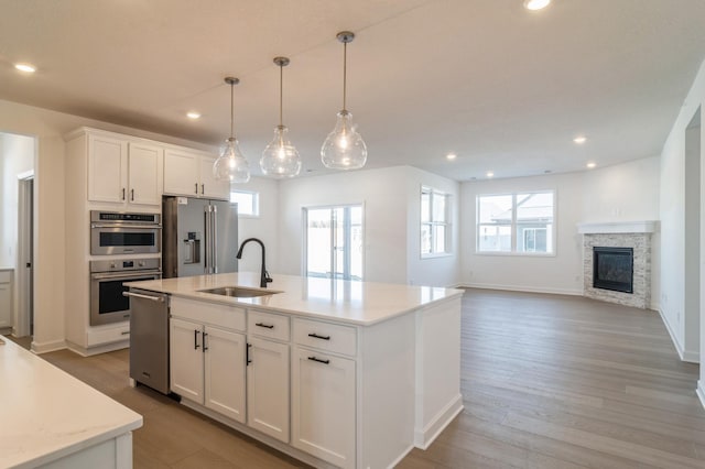 kitchen with white cabinetry, a center island with sink, hanging light fixtures, stainless steel appliances, and sink