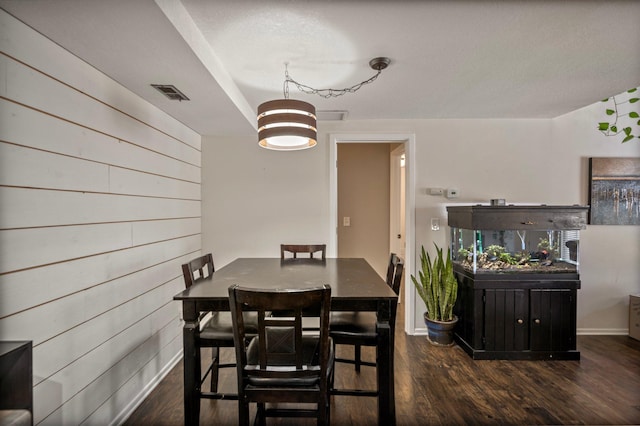 dining room featuring dark wood-style floors, wood walls, visible vents, and baseboards