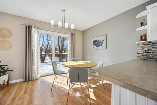 dining space with light hardwood / wood-style floors, a textured ceiling, and a notable chandelier