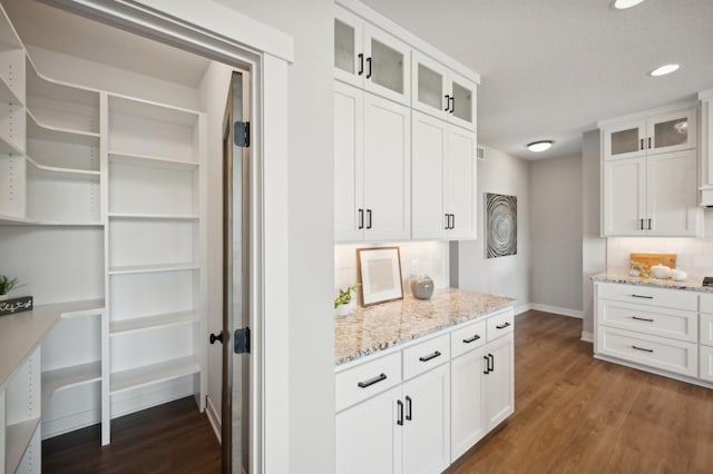 kitchen featuring decorative backsplash, white cabinetry, dark hardwood / wood-style floors, and light stone countertops