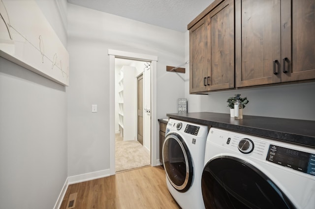 washroom featuring a textured ceiling, cabinets, light hardwood / wood-style floors, and washer and clothes dryer