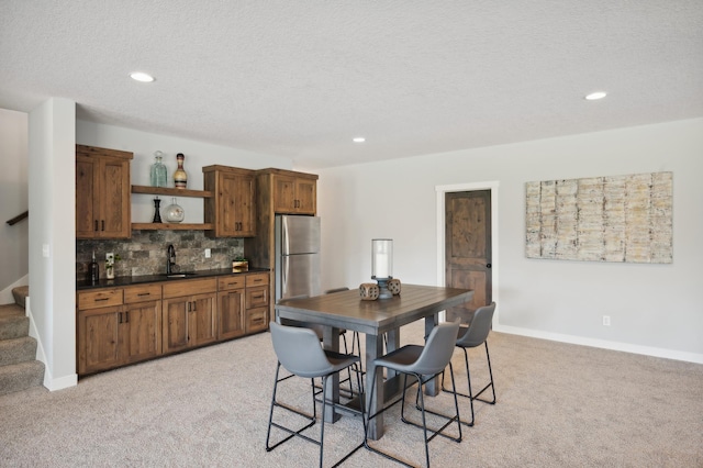 dining space featuring a textured ceiling, indoor wet bar, and light colored carpet