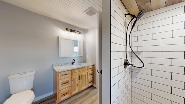 bathroom with toilet, visible vents, tiled shower, and vanity