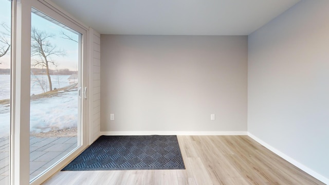 entryway with baseboards, a water view, and light wood finished floors