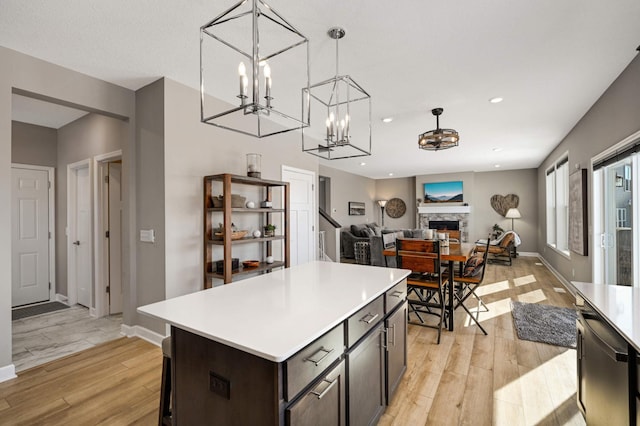 kitchen with a fireplace, dark brown cabinetry, decorative light fixtures, a kitchen island, and light hardwood / wood-style floors