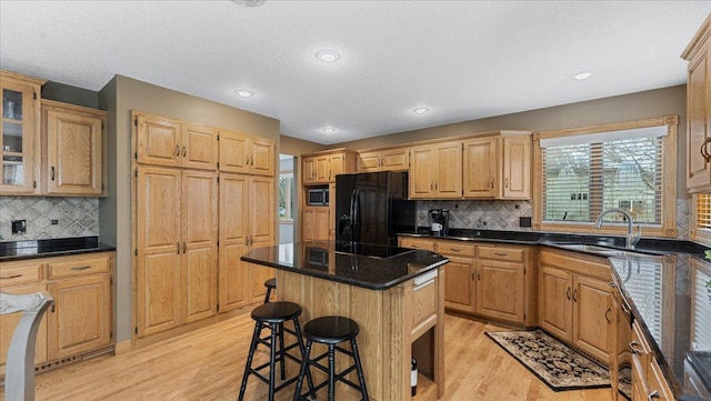 kitchen with a breakfast bar, light wood-style flooring, glass insert cabinets, a kitchen island, and black appliances