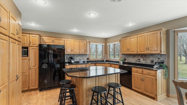 kitchen featuring a kitchen island, a kitchen breakfast bar, light wood-type flooring, black appliances, and dark countertops