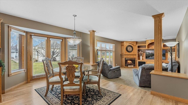 dining area with a large fireplace, light wood-style flooring, and decorative columns