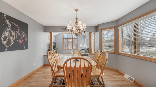 dining area featuring visible vents, a notable chandelier, light wood-style flooring, and ornate columns