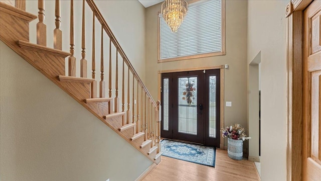 entryway featuring a towering ceiling, light wood-style floors, stairs, and a chandelier