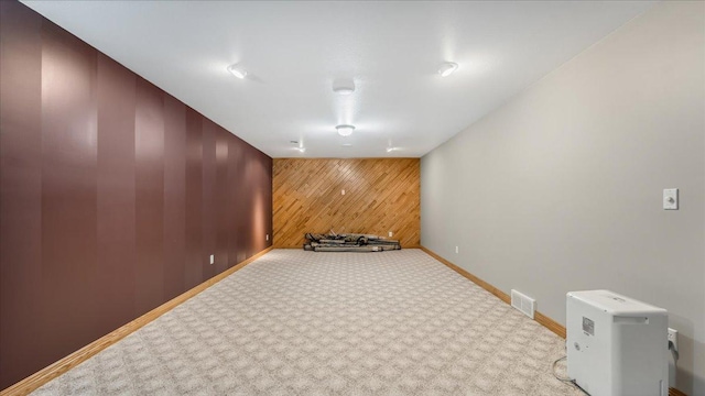 unfurnished room featuring light carpet, baseboards, visible vents, and wooden walls