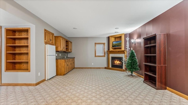 kitchen featuring a warm lit fireplace, dark countertops, freestanding refrigerator, and baseboards