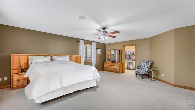 bedroom with a closet, baseboards, a ceiling fan, a walk in closet, and light colored carpet