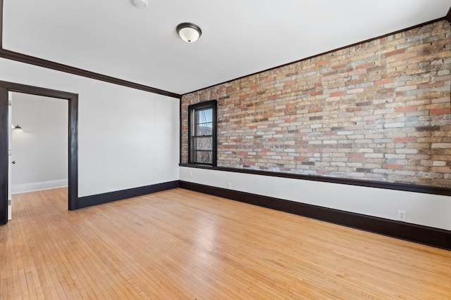 unfurnished room featuring light wood-type flooring, brick wall, baseboards, and crown molding