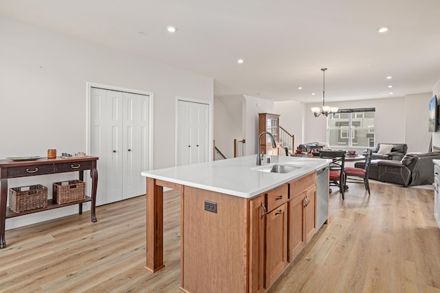 kitchen with dishwasher, pendant lighting, a kitchen island with sink, and light wood-type flooring