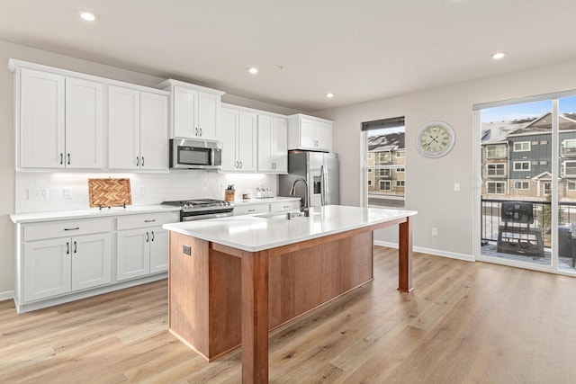 kitchen with tasteful backsplash, stainless steel appliances, an island with sink, sink, and white cabinetry