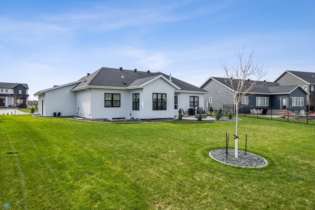 rear view of property with board and batten siding, roof with shingles, a lawn, a patio area, and fence