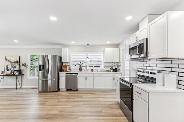 kitchen featuring appliances with stainless steel finishes, backsplash, light wood-type flooring, white cabinetry, and pendant lighting