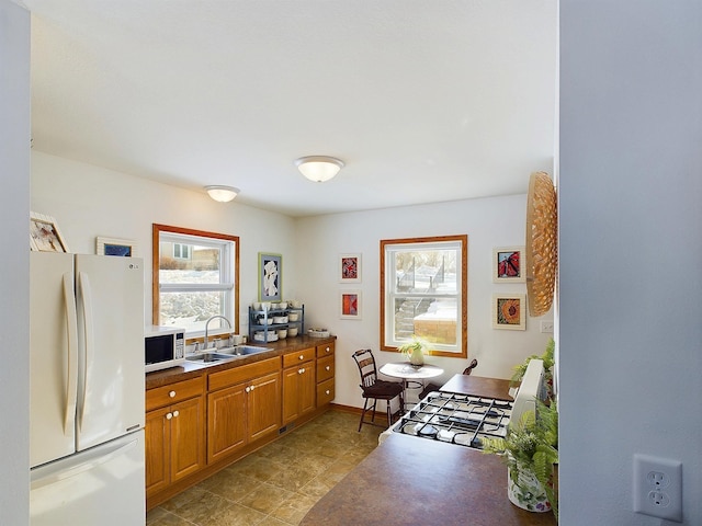 kitchen with brown cabinets, dark countertops, stove, freestanding refrigerator, and a sink