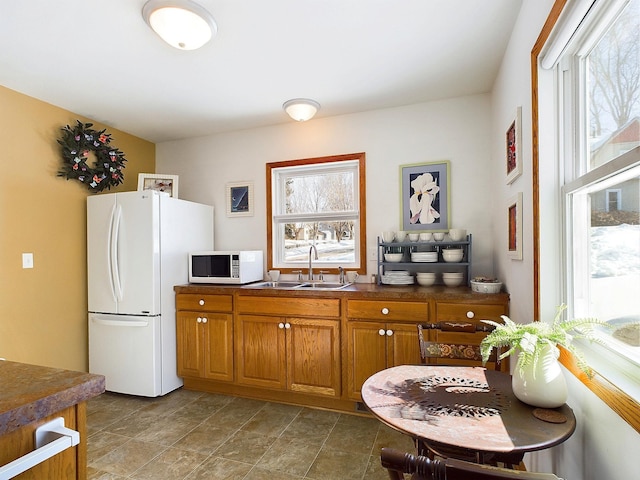 kitchen with dark countertops, white appliances, a wealth of natural light, and a sink