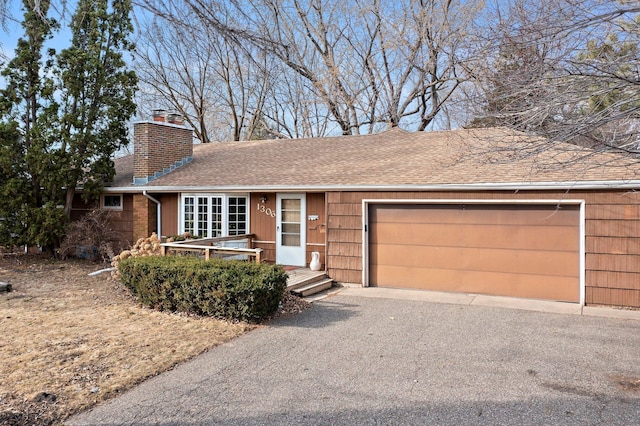 ranch-style house with a shingled roof, aphalt driveway, an attached garage, and a chimney