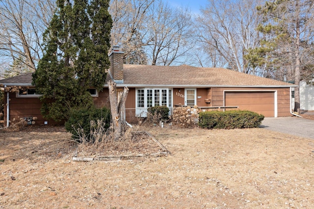 single story home with driveway, roof with shingles, a chimney, and an attached garage