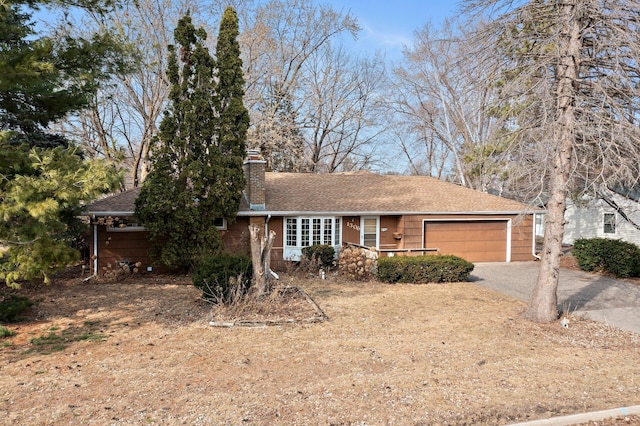 single story home with an attached garage, a chimney, driveway, and a shingled roof