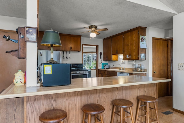 kitchen with visible vents, ceiling fan, light wood-style flooring, a peninsula, and stainless steel stove