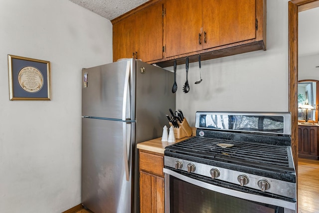 kitchen with light wood finished floors, light countertops, stainless steel appliances, brown cabinetry, and a textured ceiling