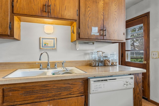 kitchen featuring light countertops, brown cabinetry, white dishwasher, and a sink