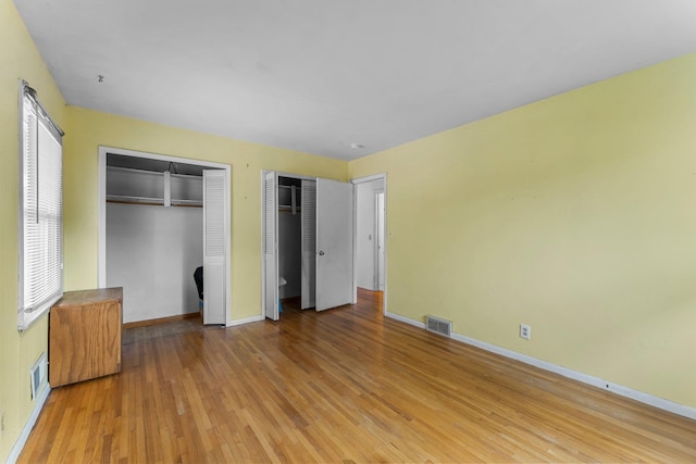 unfurnished bedroom with visible vents, baseboards, two closets, and wood finished floors