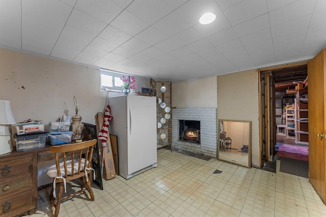 basement featuring tile patterned floors, a fireplace, and freestanding refrigerator