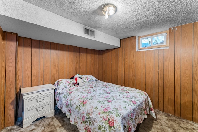 bedroom featuring visible vents, wooden walls, carpet flooring, and a textured ceiling