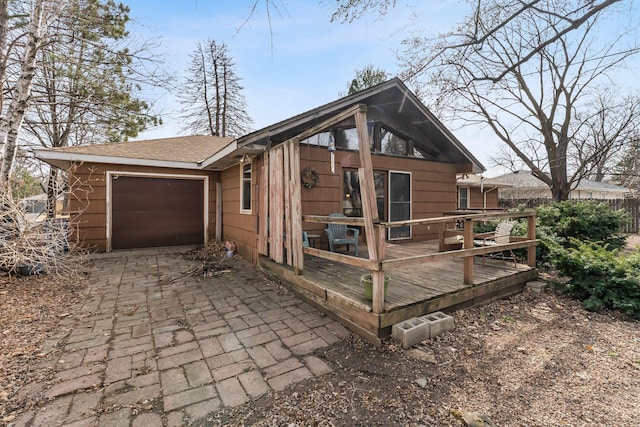 view of side of property featuring a deck, a garage, driveway, and a shingled roof