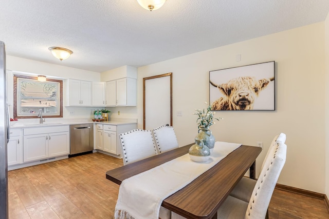 dining room featuring sink, a textured ceiling, and light hardwood / wood-style floors