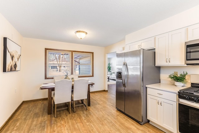 kitchen with white cabinetry, a textured ceiling, stainless steel appliances, and light hardwood / wood-style floors