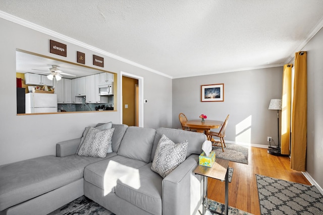 living area featuring a ceiling fan, baseboards, ornamental molding, light wood-style floors, and a textured ceiling